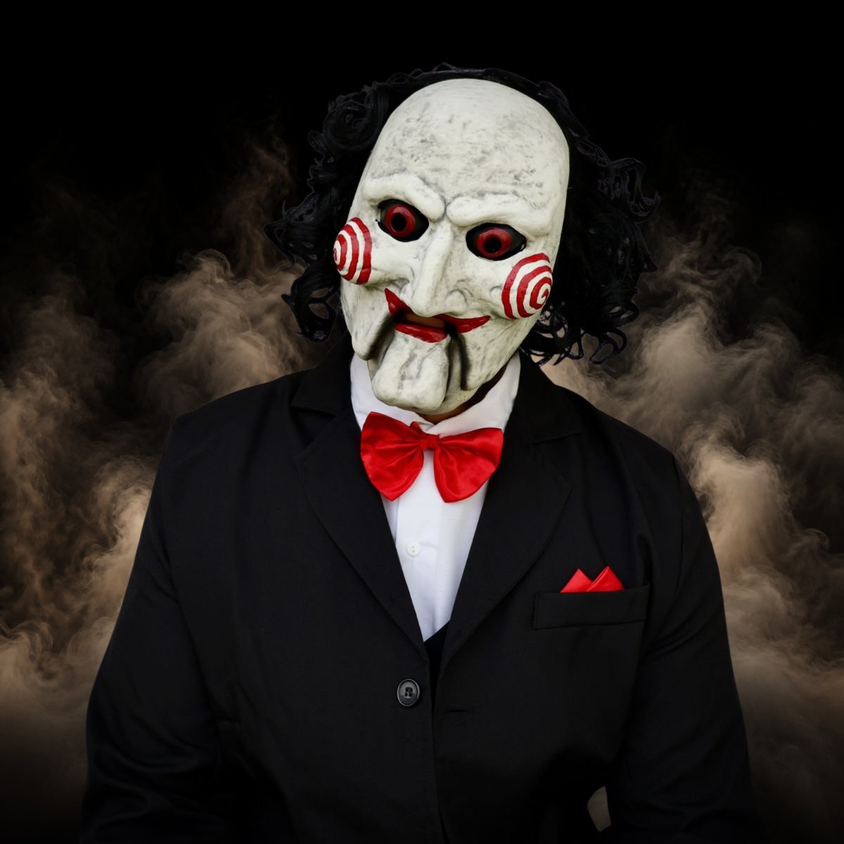 Creepy puppet halloween mask with red spiral cheeks worn with a black suit and red bow tie