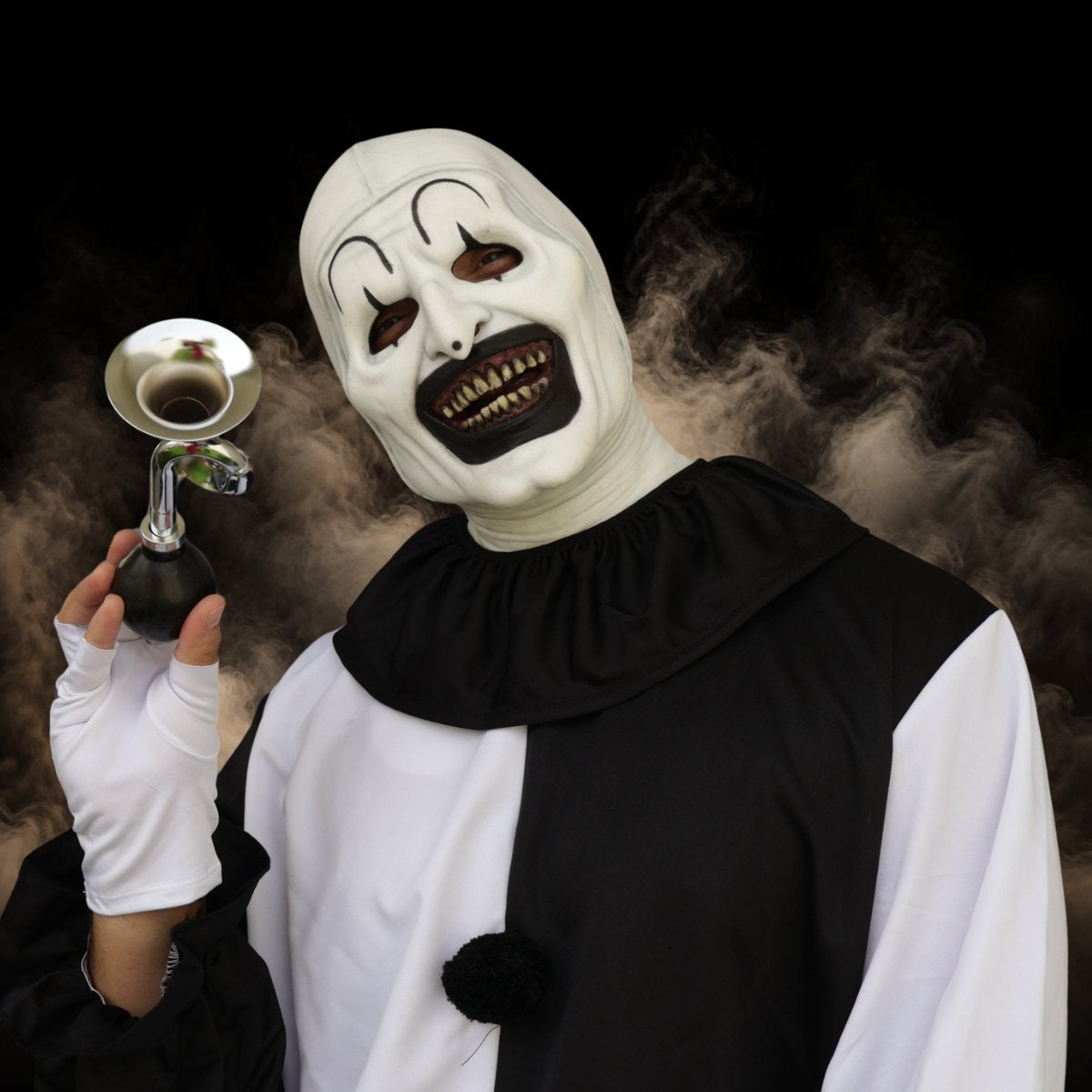 Silent clown mask holding a small brass horn in a black and white costume